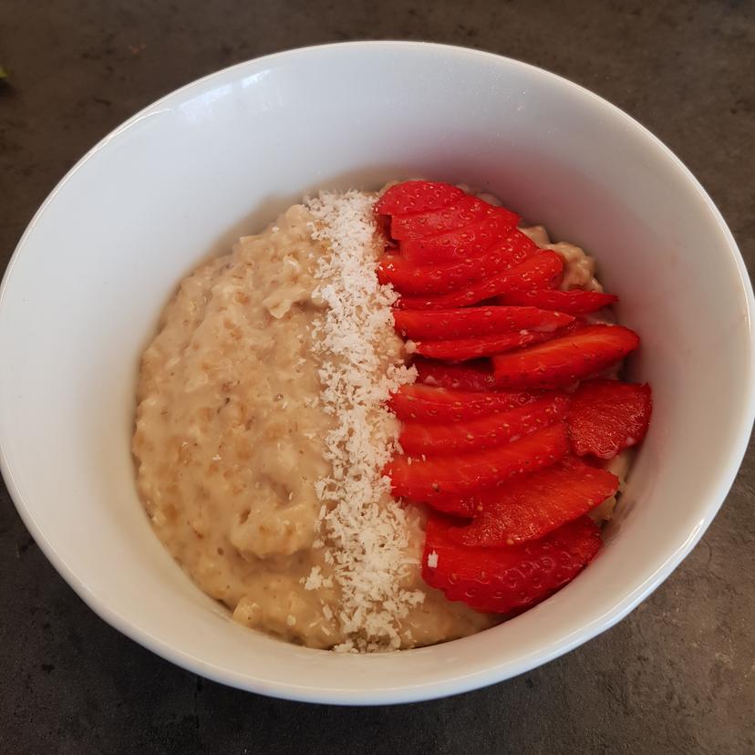 Porridge déposé dans un bol avec toppings fraises et noix de coco 