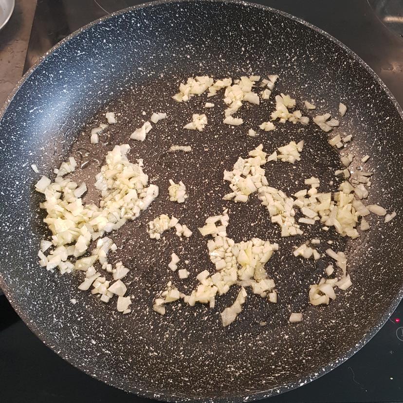 Ail et oignon en train de cuire avec un  filet d'huile d'olive dans une poêle 