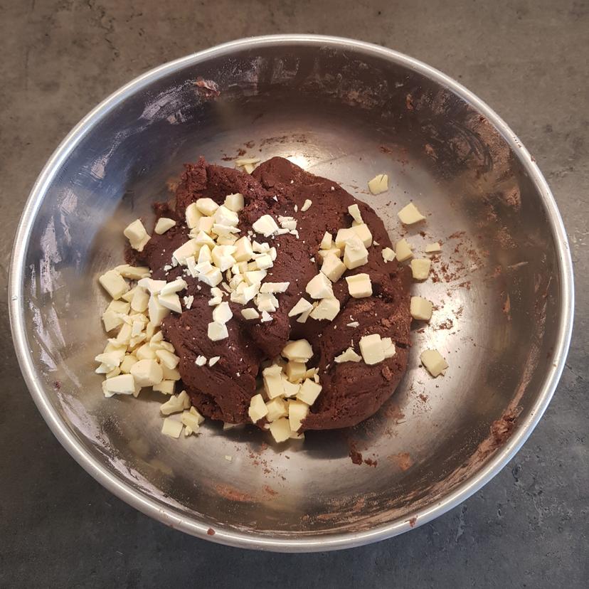 Ensemble des ingrédients mélangés formant une pâte à cookies homogène avec ajout des pépites de chocolat blanc